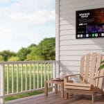 Proofvision - A cozy porch with a wooden Adirondack chair and matching side table. On the table are a coffee cup and saucer. A large plant and a watering can sit beside the chair. A TV mounted on the wall is displaying the "Stranger Things" screen. Greenery is visible in the background.