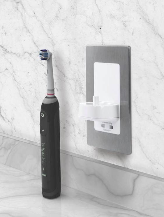 Proofvision - A black electric toothbrush is standing on a marble countertop against a matching marble backsplash. The toothbrush is positioned next to a gray and white wall-mounted charger with a plug socket.